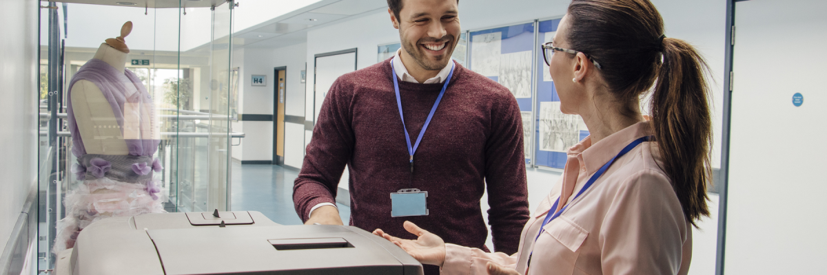 Two teachers are talking while standing at a printer in the school hall.